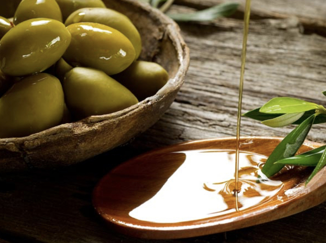 bowl of green olives and glass jar pouring out olive oil